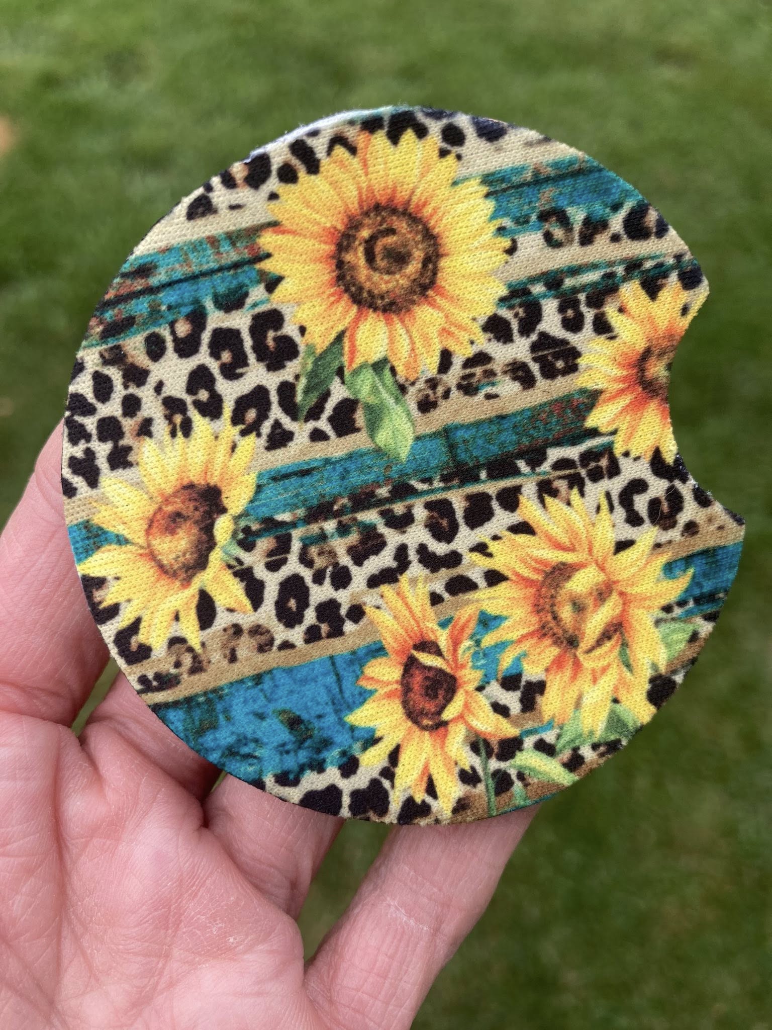 Round coaster with sunflower and leopard print design held in a hand against a green background