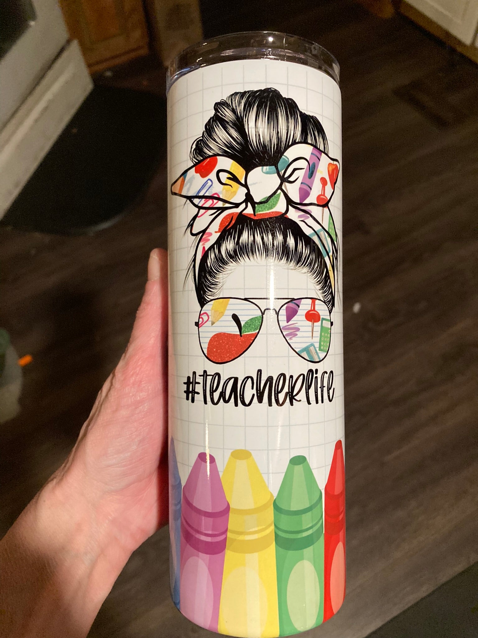 Tumbler with a design of a woman with a bun, sunglasses, and colorful crayons with '#teacherlife' text. White tumbler featuring messy bun teacher design with glasses, colorful crayons, and #teacherlife text