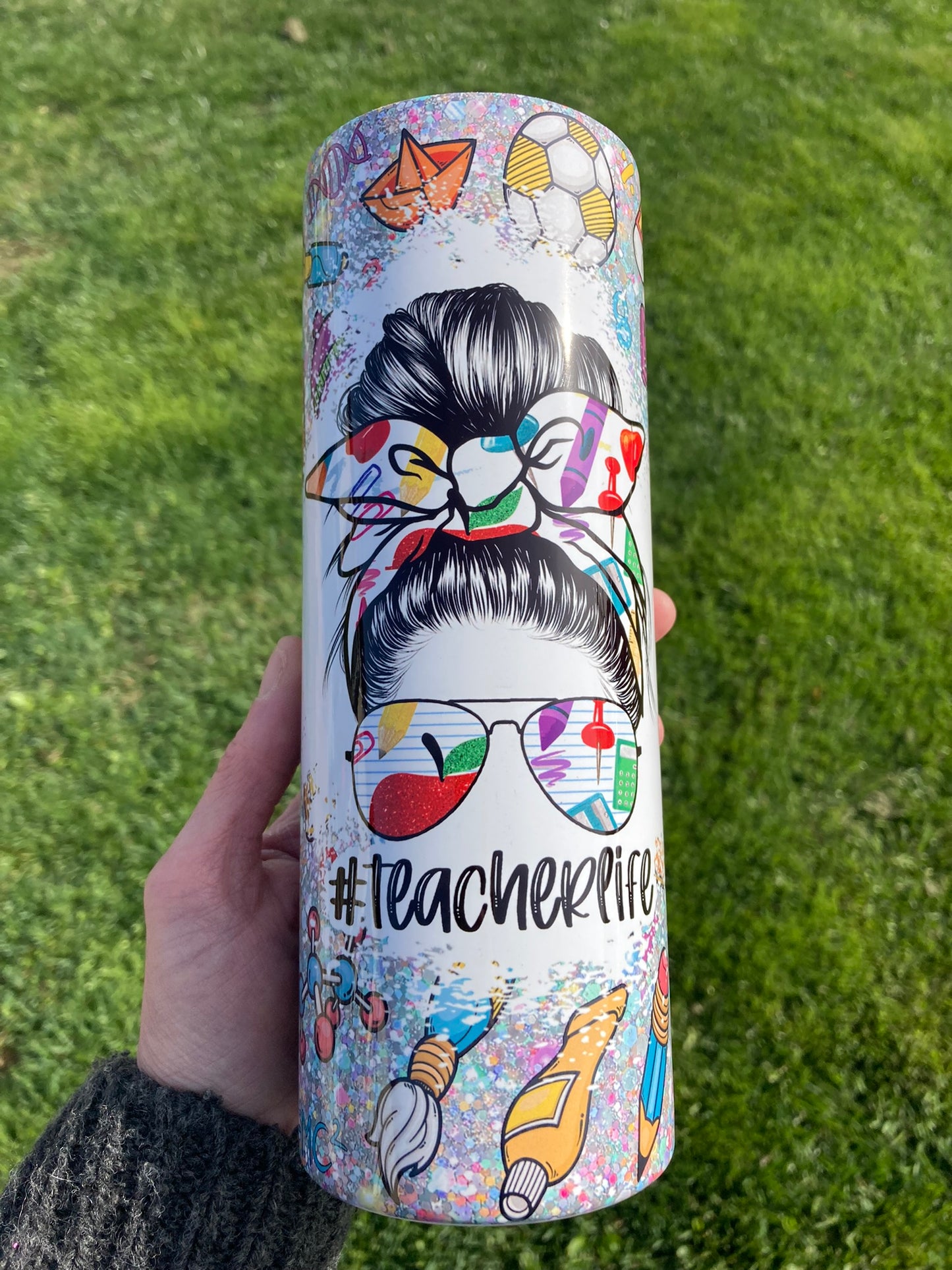 20oz tumbler with #teacherlife messy bun illustration and colorful classroom supply icons. Teacher Life Rainbow Classroom Icons 20oz Tumbler. 