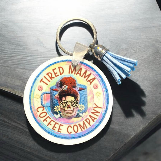 Tired Mama Coffee Co Keychain. 2.5 x 2.5 the image is a skeleton messy bun mama with a blue coffee mug. 