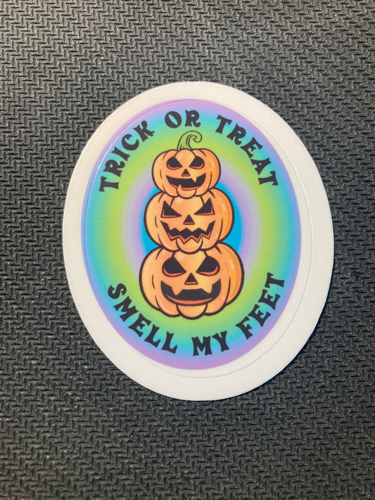 Round sticker with three stacked jack-o’-lantern pumpkins and rainbow background text “Trick or Treat Smell My Feet.”