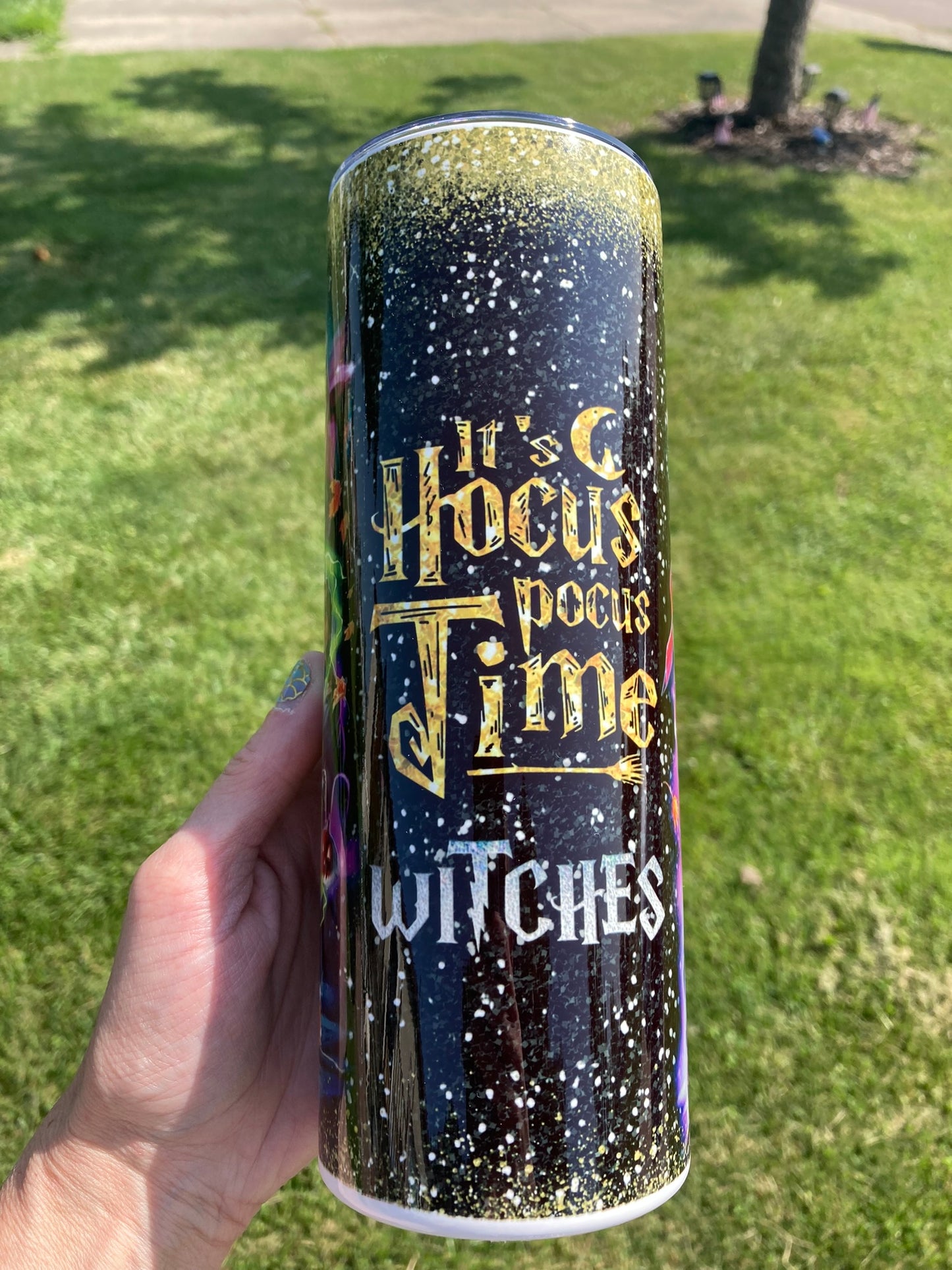 Tumbler with 'It's Hocus Pocus Time Witches' text held in front of a grassy background. 