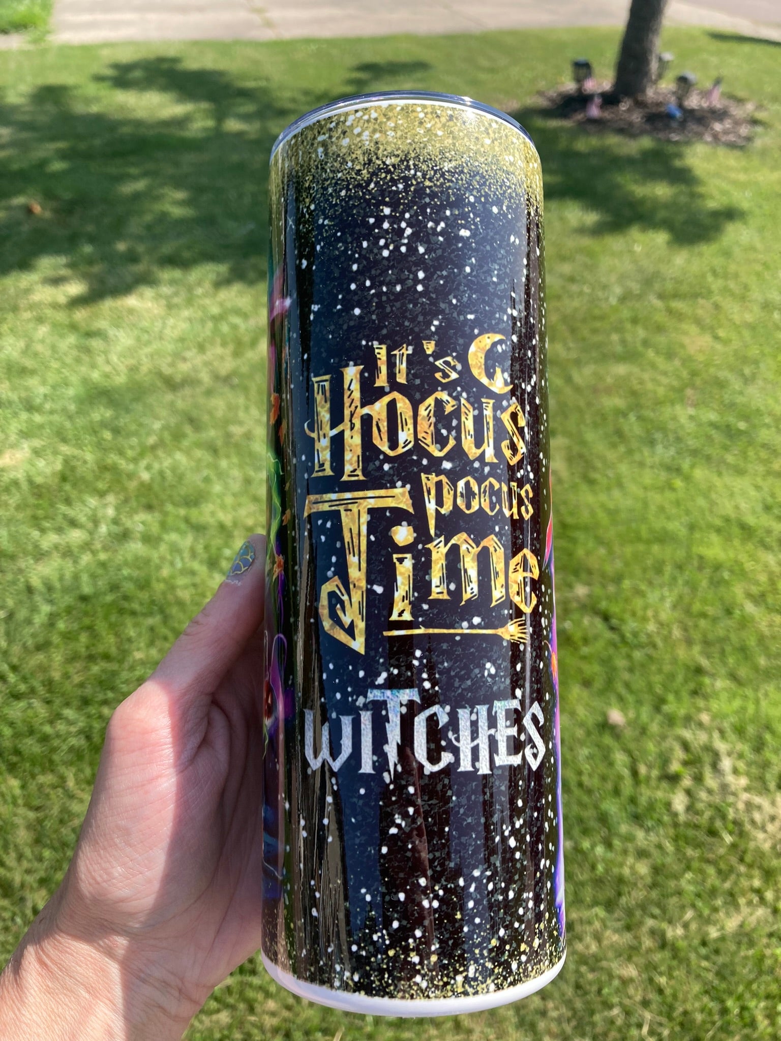Tumbler with 'It's Hocus Pocus Time Witches' text held in front of a grassy background. 