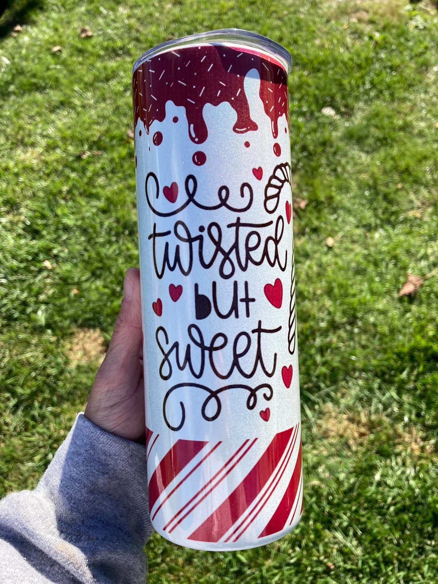 Tumbler with 'twisted but sweet' text and candy cane design held in a hand against a grass background