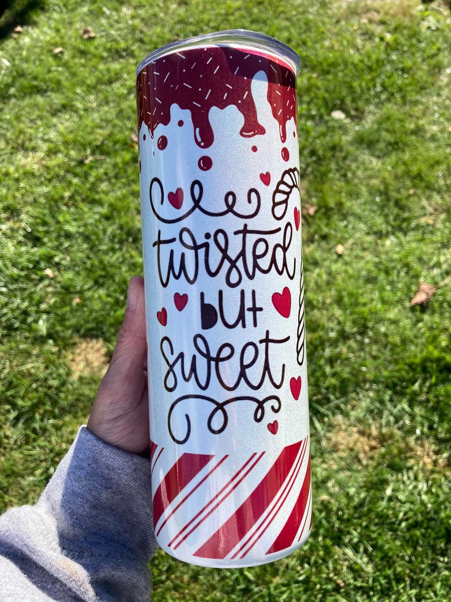 Tumbler with 'twisted but sweet' text and candy cane design held in a hand against a grass background