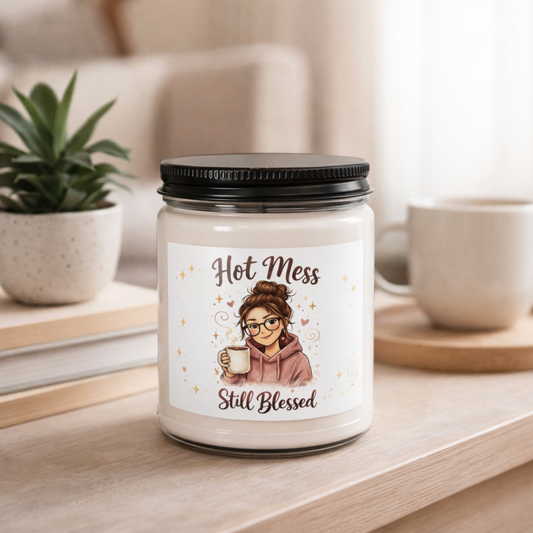Candle jar with a label featuring an illustration of a woman and text 'Hot Mess Still Blessed' on a table.